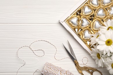 Photo of Delicious heart shaped chocolate candies, scissors and twine on white wooden table, flat lay. Space for text