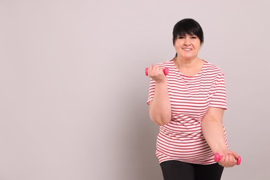 Photo of Happy overweight mature woman doing exercise with dumbbells on grey background, space for text