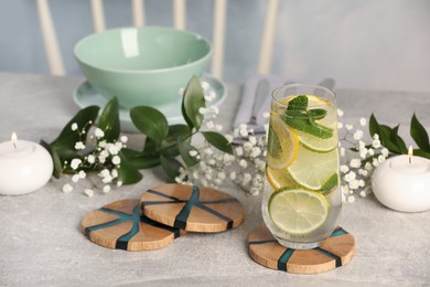 Glass of lemonade and stylish wooden cup coasters on light table