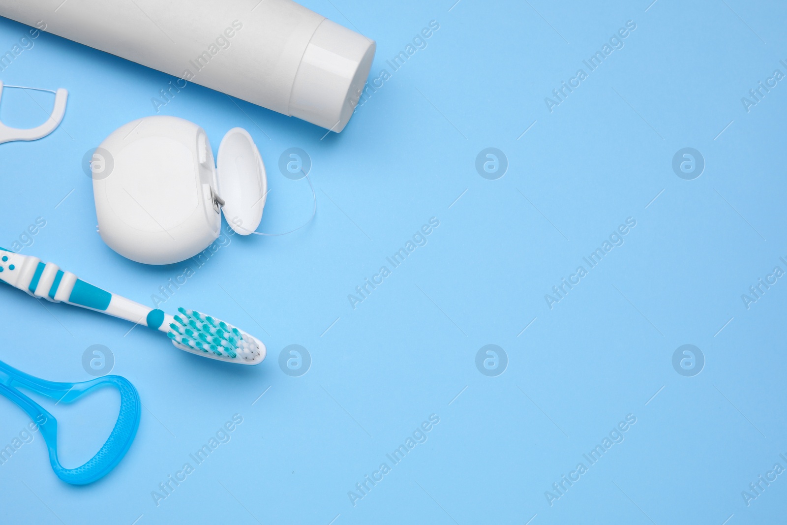 Photo of Tongue cleaner and other oral care products on light blue background, flat lay. Space for text