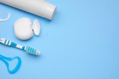 Photo of Tongue cleaner and other oral care products on light blue background, flat lay. Space for text