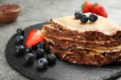 Photo of Delicious thin pancakes with chocolate paste and berries on slate plate, closeup
