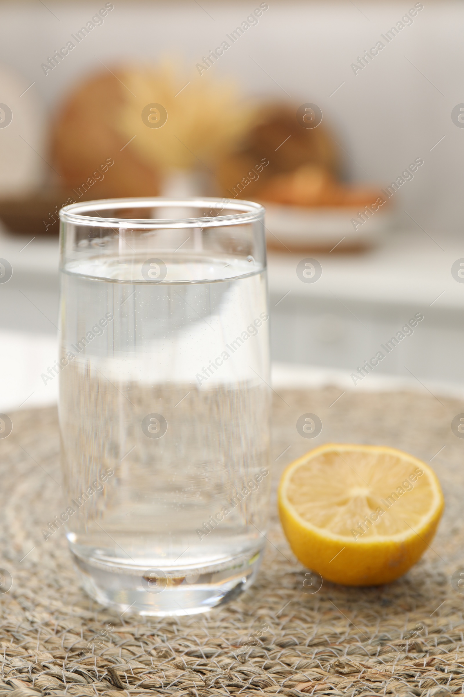 Photo of Glass with clear water and half of lemon on table in kitchen