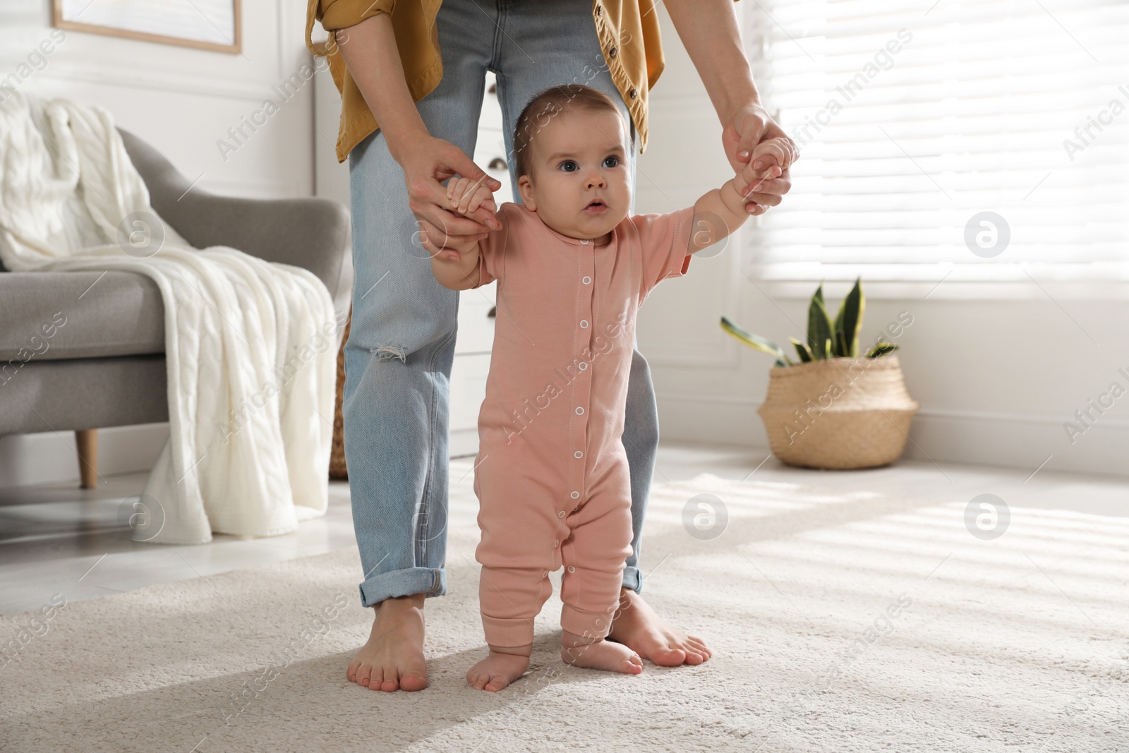 Photo of Mother supporting her baby daughter while she learning to walk at home