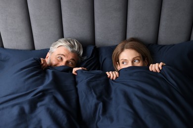 Photo of Lovely mature couple hiding together under blanket in bed at home, above view