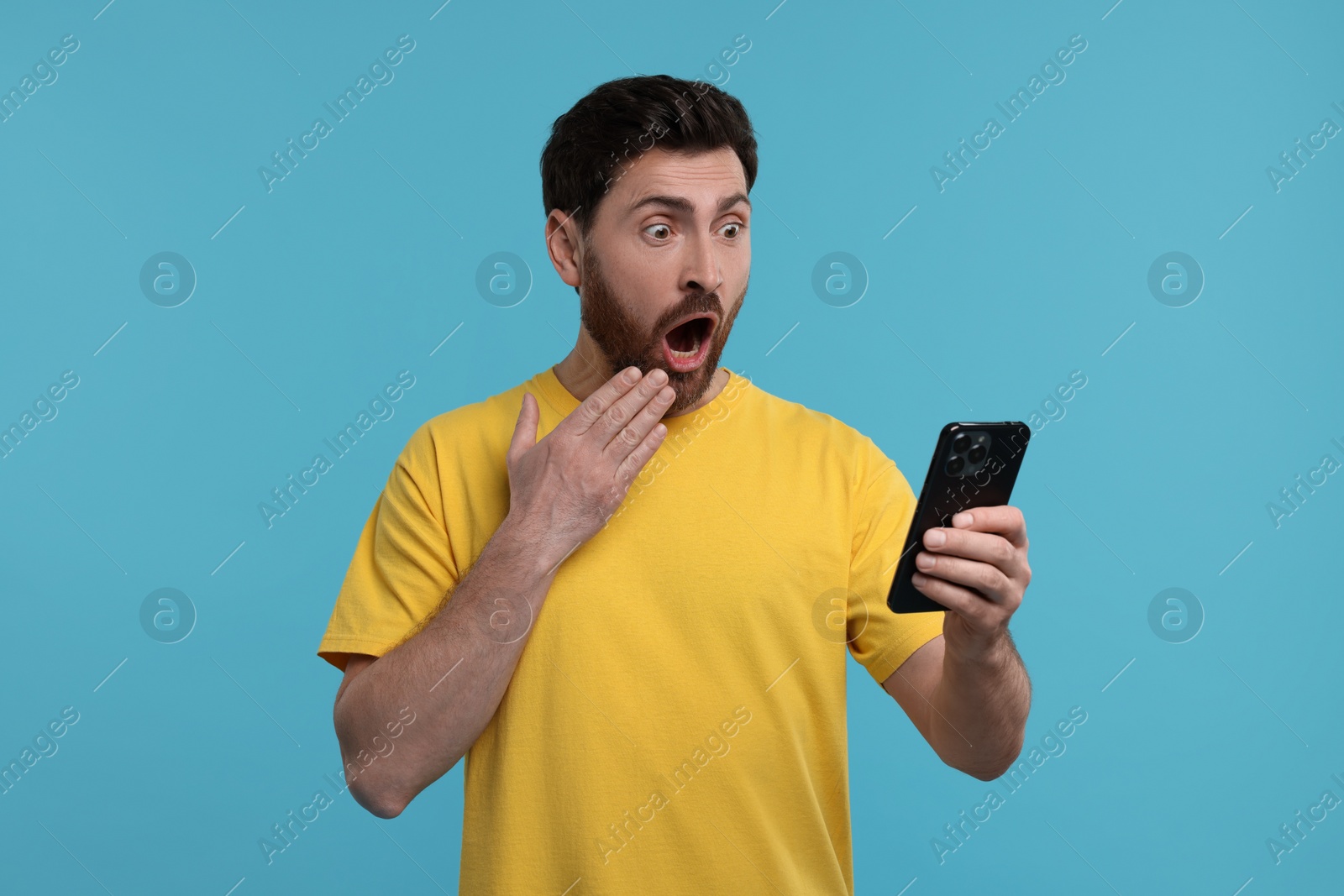 Photo of Surprised man with smartphone on light blue background