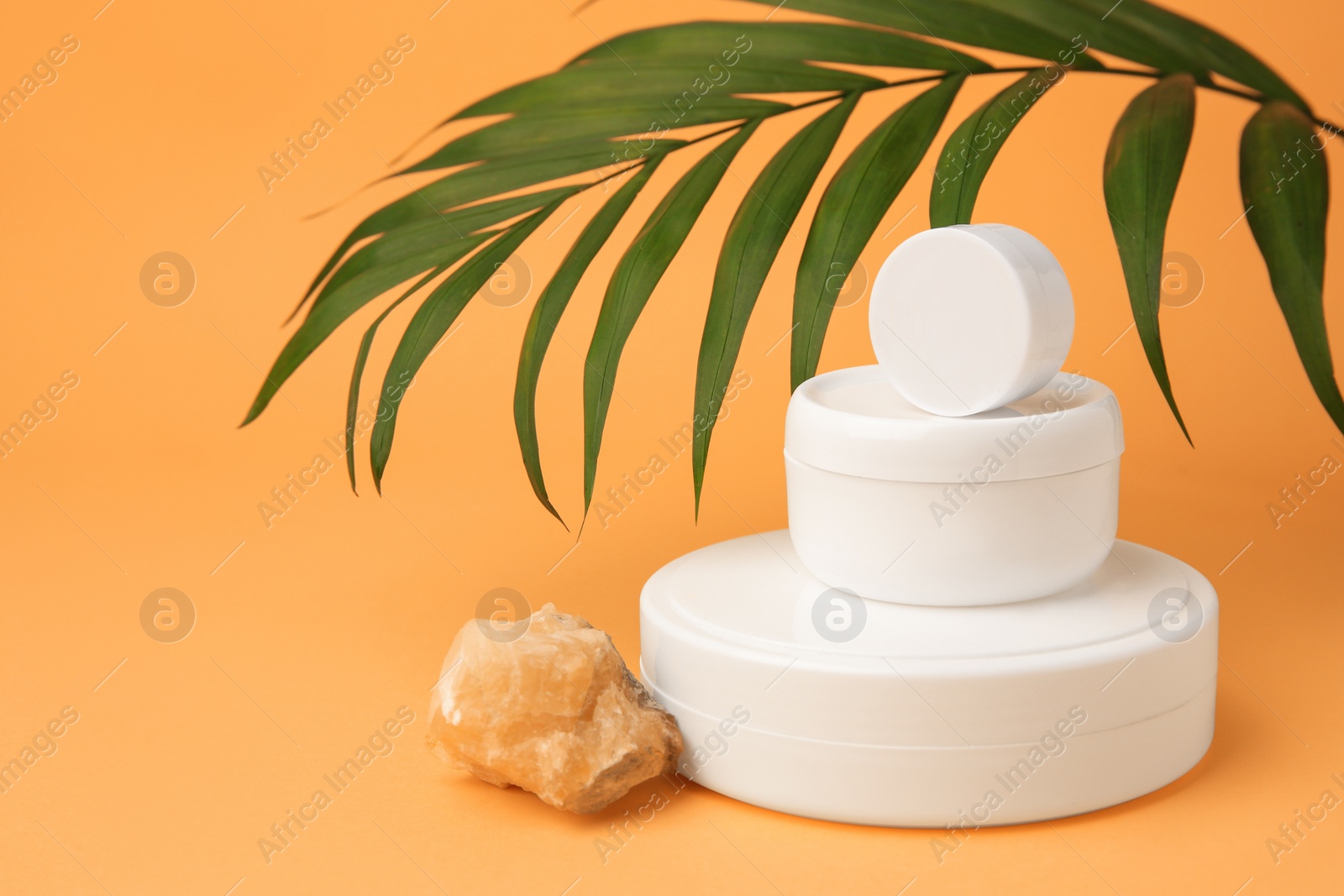 Photo of Cosmetic products, quartz gemstone and palm leaf on orange background, space for text