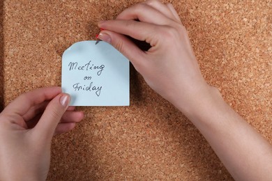Photo of Woman pinning paper note with phrase Meeting On Friday to cork board, closeup