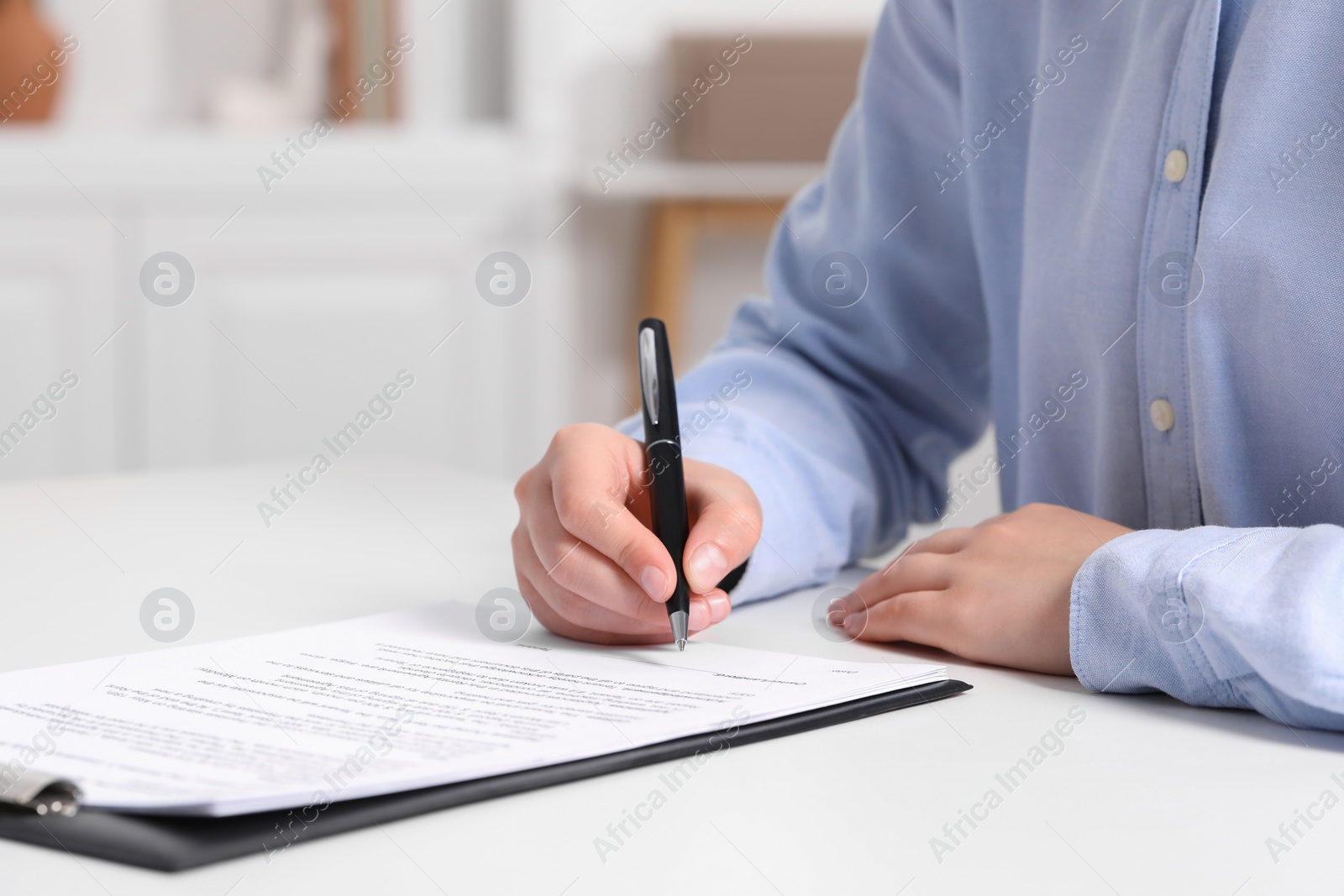 Photo of Woman signing document at white table indoors, closeup. Space for text