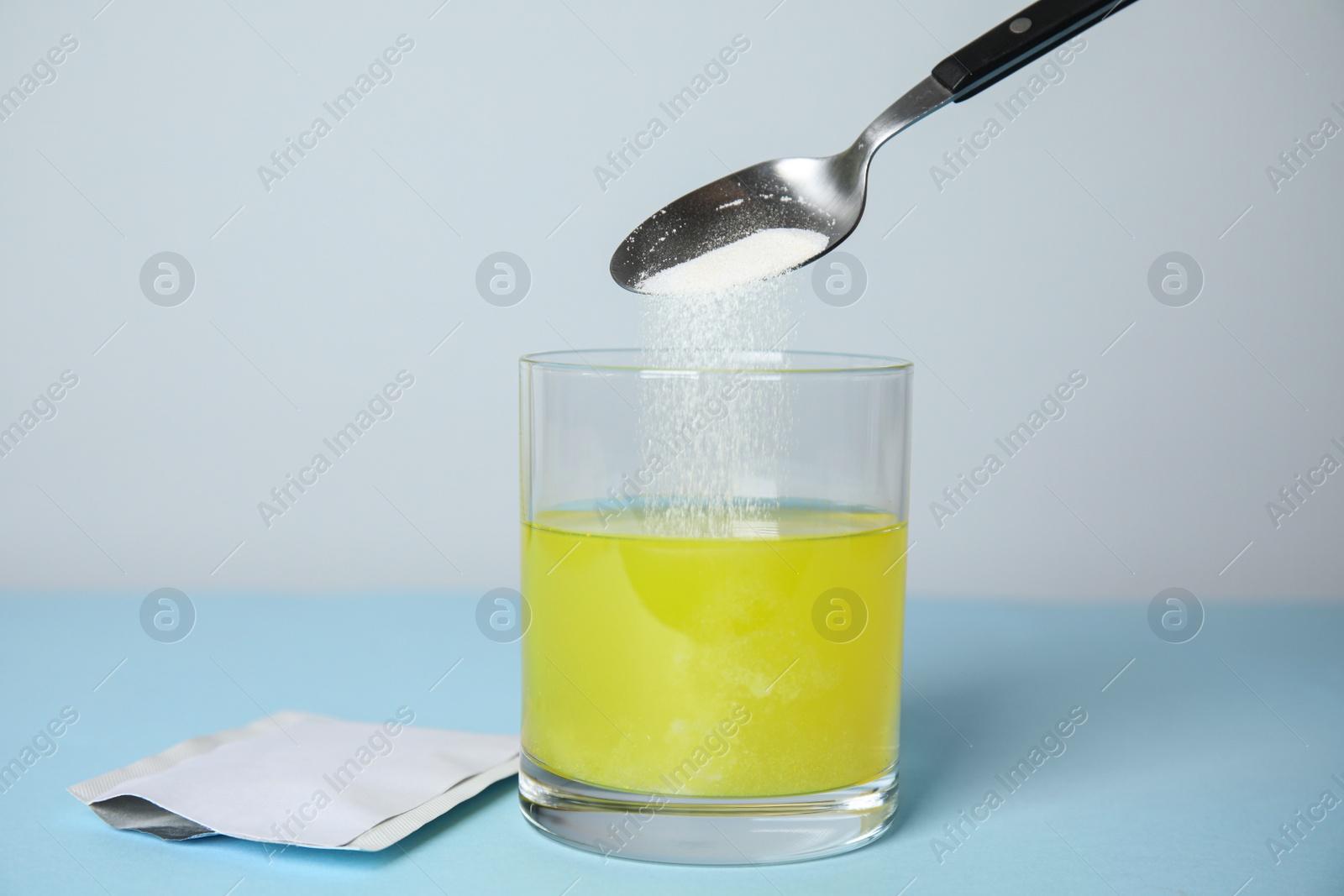 Photo of Pouring medicine into glass of water near sachet on turquoise table