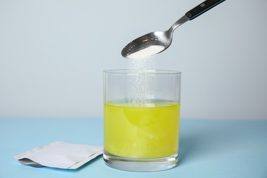 Pouring medicine into glass of water near sachet on turquoise table