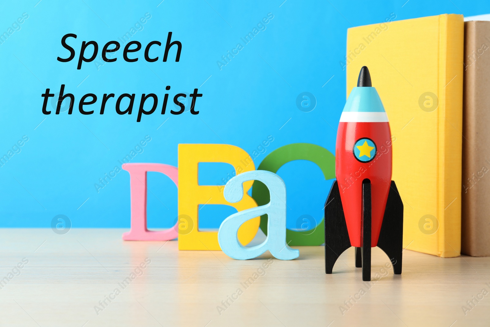 Image of School books and rocket on wooden table and text Speech Therapist against light blue background 