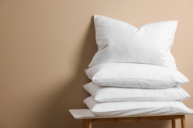 Photo of Stack of soft white pillows on table near beige wall. Space for text
