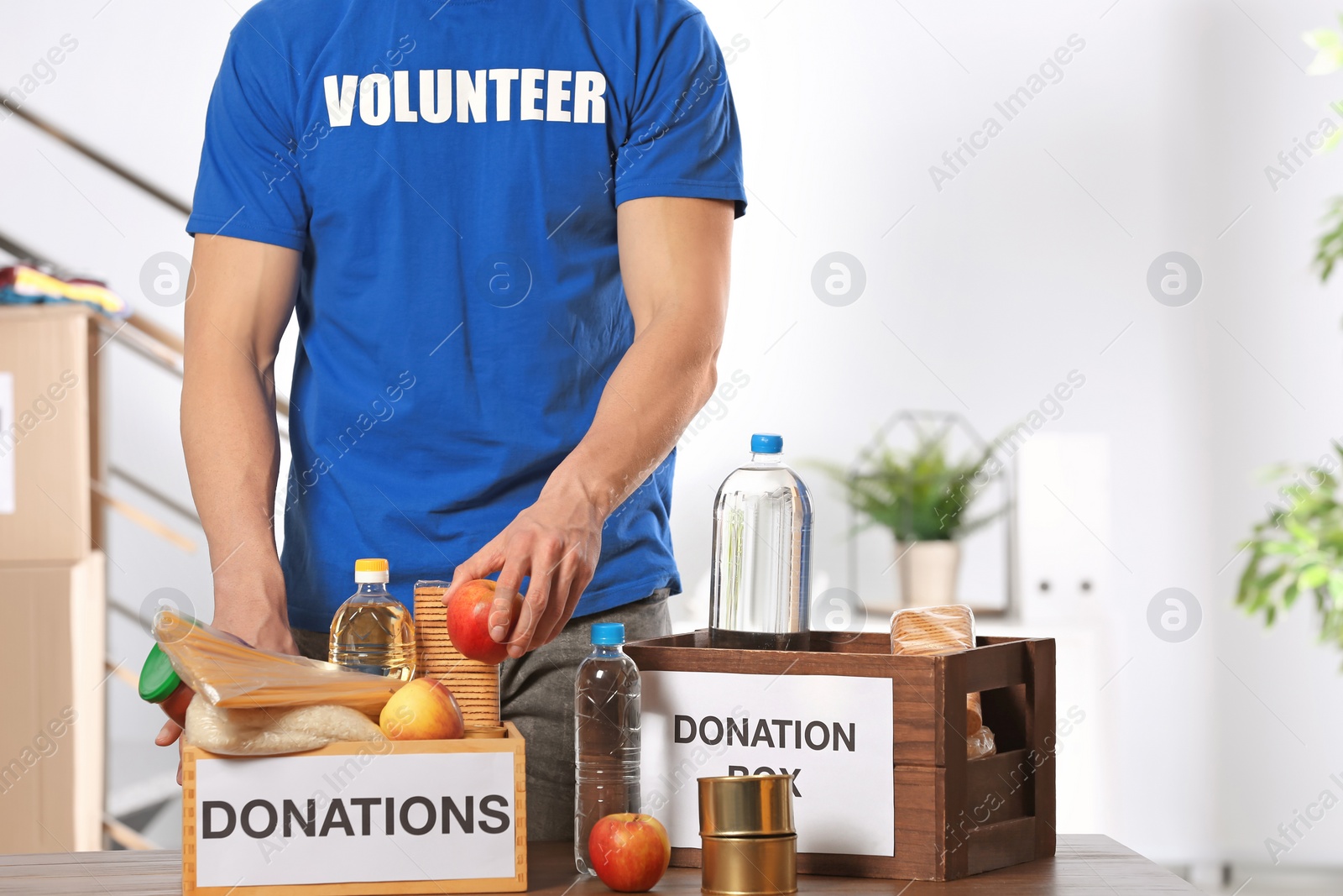 Photo of Male volunteer putting food products in donation boxes indoors