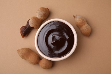 Photo of Bowl of tamarind sauce and fresh pods on light brown table, flat lay