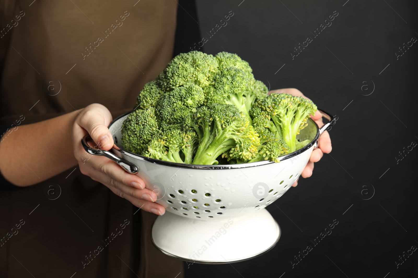 Photo of Woman holding colander with fresh green broccoli on black background, closeup