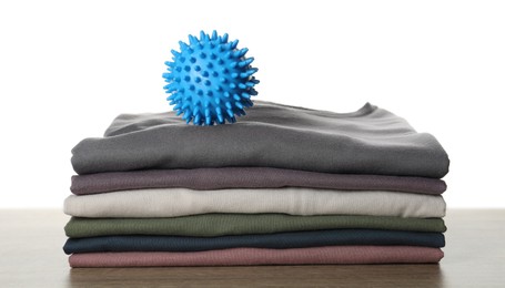 Photo of Blue dryer ball and stacked clean clothes on wooden table against white background