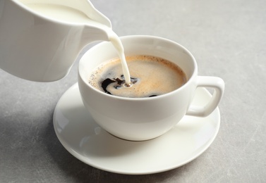 Pouring milk into cup of hot coffee on grey table