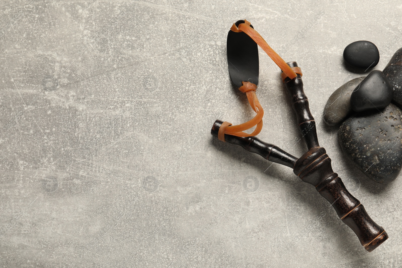 Photo of Black slingshot with stones on light grey table, flat lay. Space for text