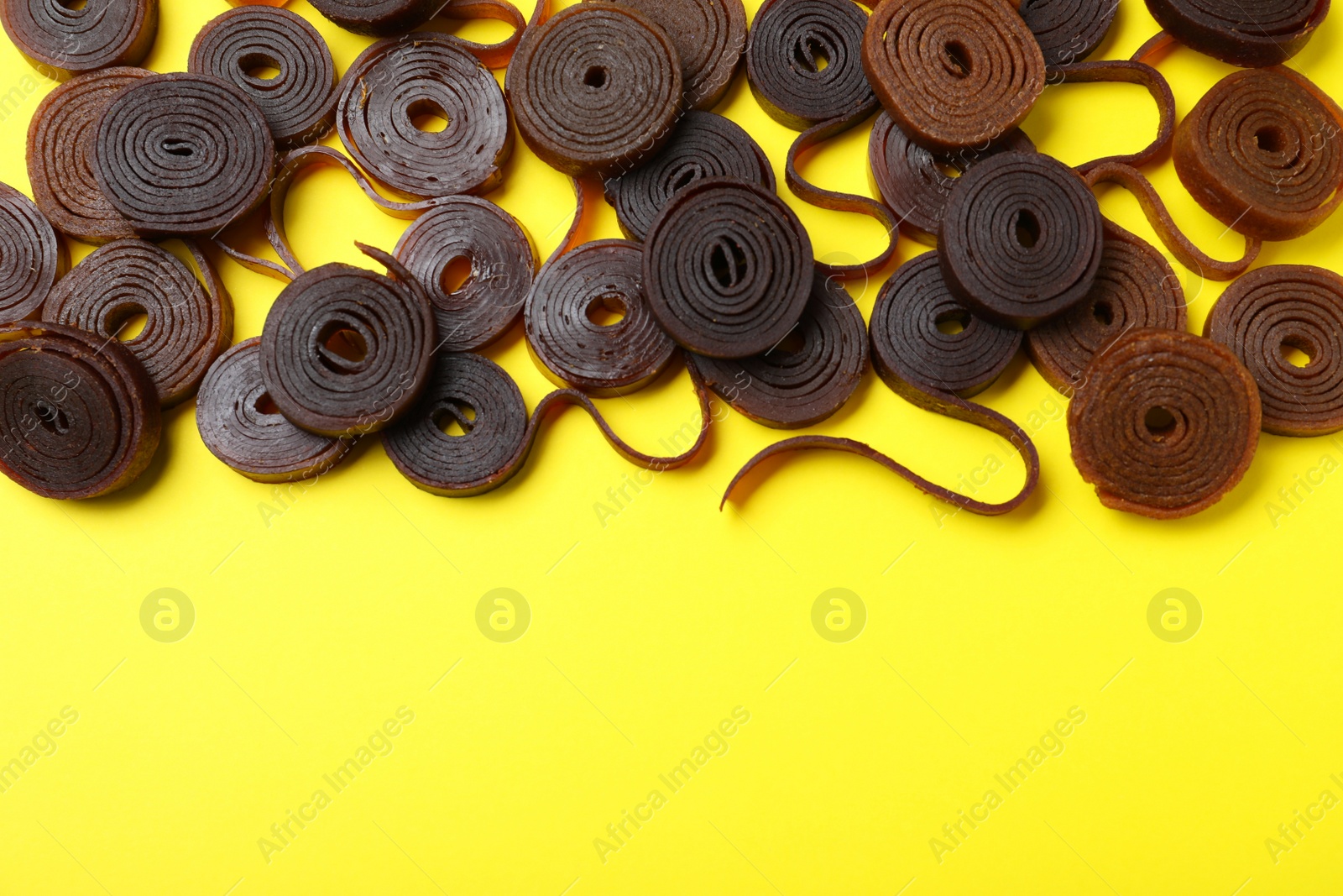 Photo of Delicious fruit leather rolls on yellow background, flat lay. Space for text