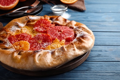 Photo of Delicious galette with citrus fruits on blue wooden table, closeup