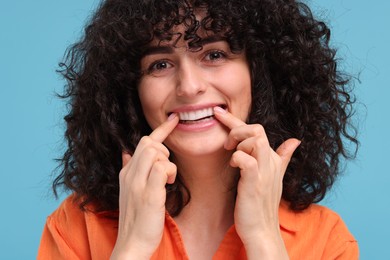 Young woman applying whitening strip on her teeth against light blue background