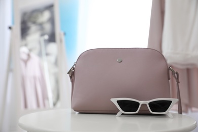 Photo of Stylish woman's bag and sunglasses on table in room
