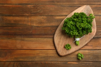 Photo of Bunch of fresh curly parsley on wooden table, flat lay. Space for text