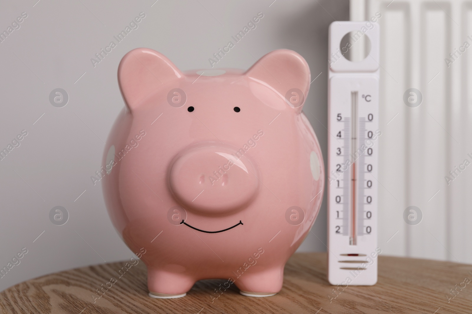 Photo of Piggy bank with thermometer on wooden table near heating radiator