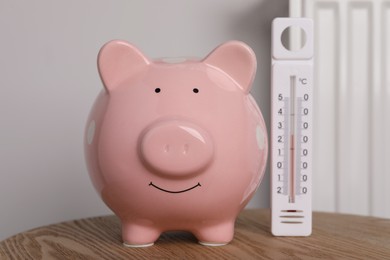 Photo of Piggy bank with thermometer on wooden table near heating radiator