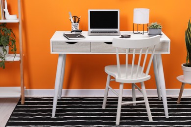 Workplace with laptop, stationery on desk and chair in home office