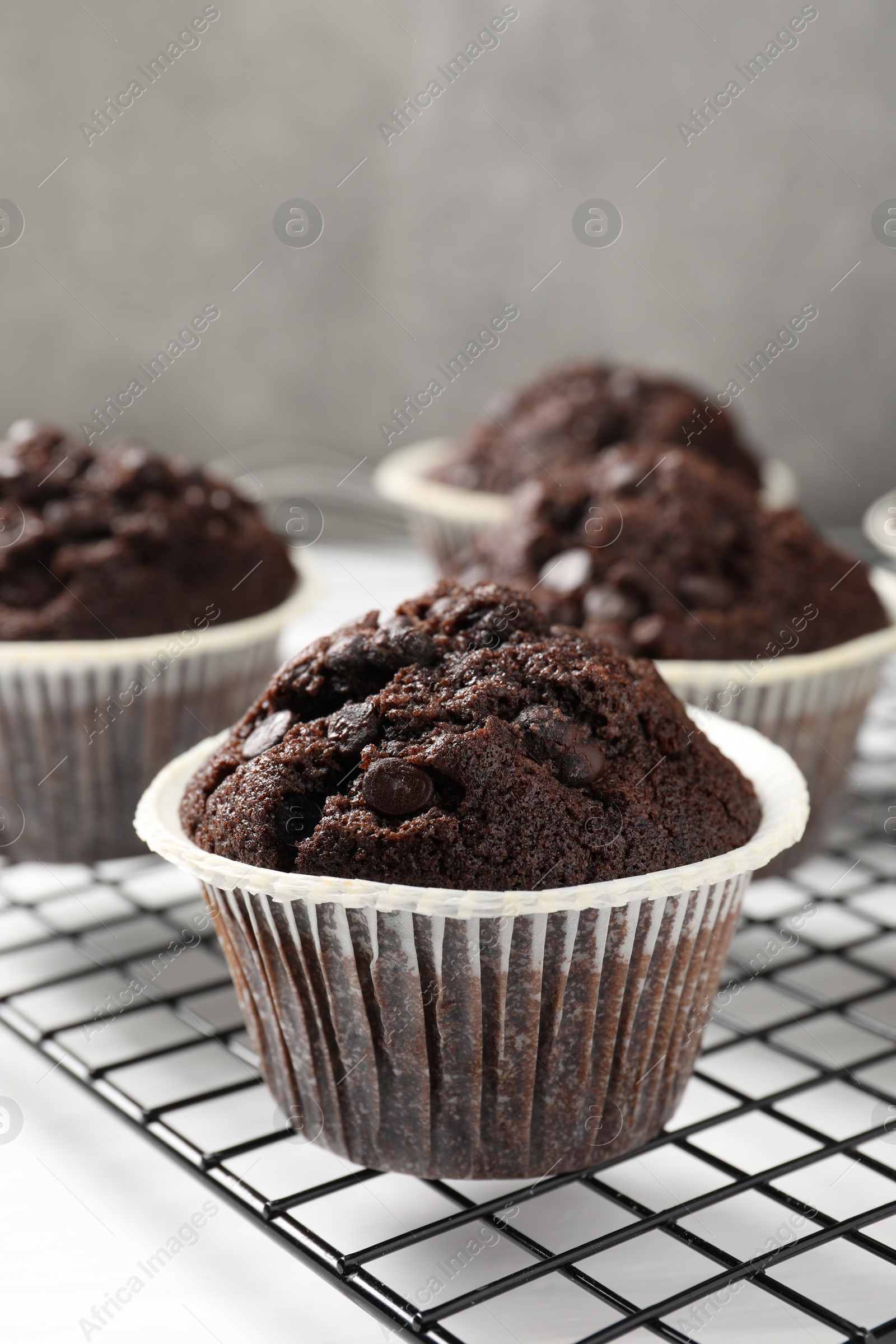 Photo of Tasty chocolate muffins and cooling rack on white table, closeup