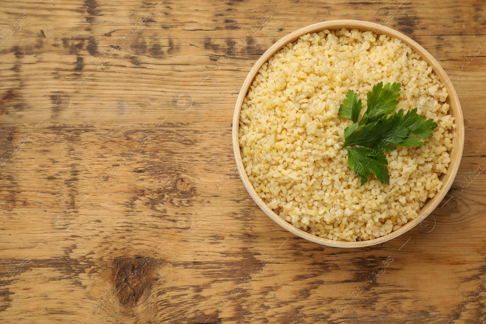 Photo of Delicious bulgur with parsley on wooden table, top view. Space for text