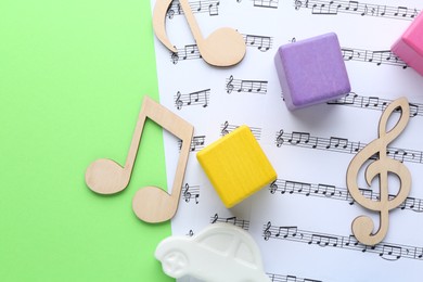 Wooden notes, music sheets and toys on light green background, top view with space for text. Baby song concept