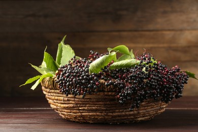 Photo of Ripe elderberries with green leaves in wicker basket on wooden table