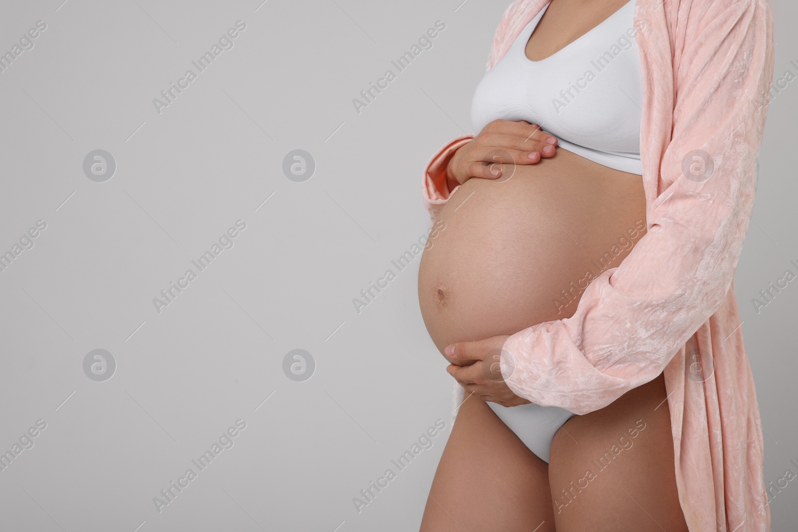 Photo of Pregnant woman in stylish comfortable underwear and robe on grey background, closeup. Space for text