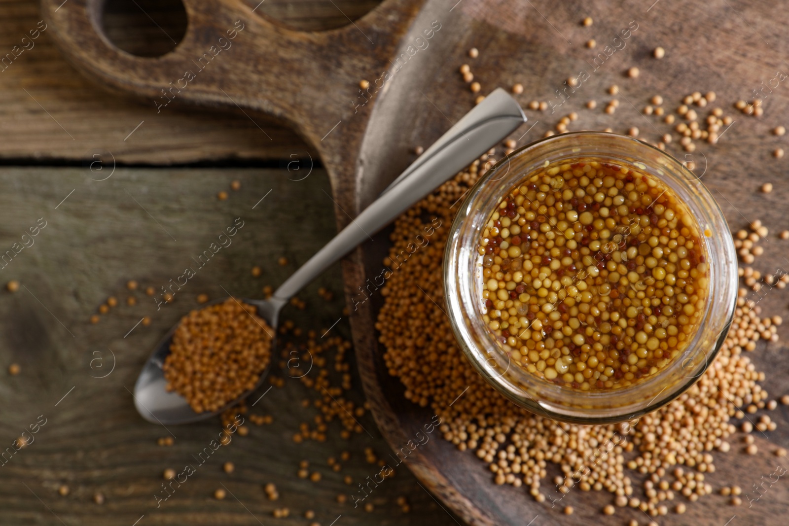 Photo of Jar and spoon of whole grain mustard on wooden table, flat lay. Space for text