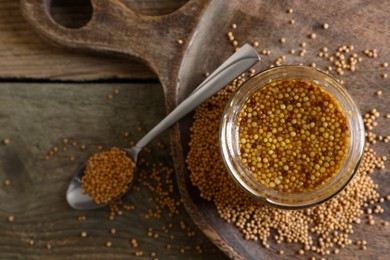 Jar and spoon of whole grain mustard on wooden table, flat lay. Space for text