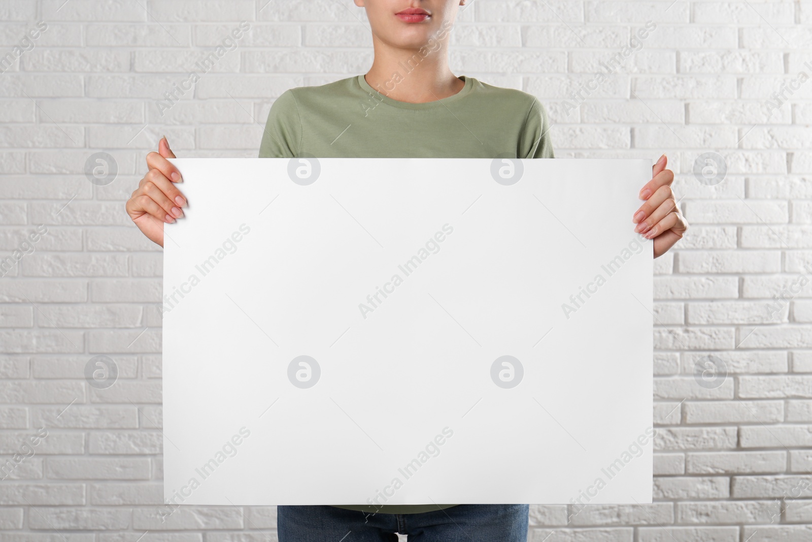 Photo of Woman holding blank poster near white brick wall, closeup. Mockup for design