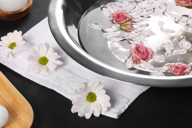 Photo of Bowl of water with flowers on dark table, closeup. Pedicure procedure
