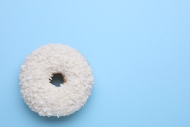 Tasty glazed donut with coconut shavings on light blue background, top view. Space for text