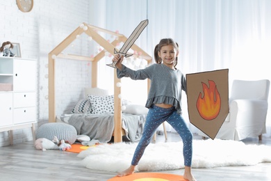 Cute little girl playing with cardboard armor in bedroom