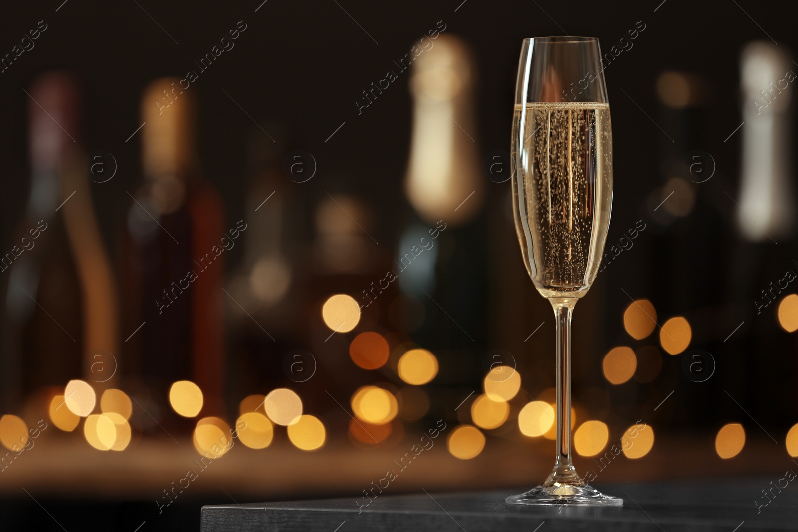 Photo of Glass of champagne on table against blurred background. Space for text