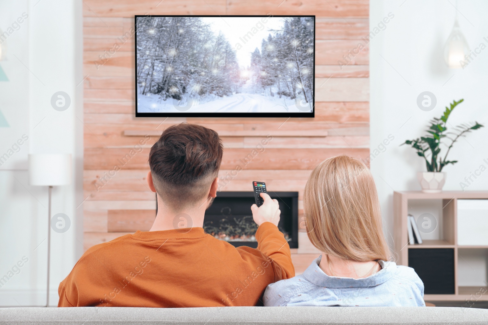 Image of Couple watching TV on sofa in living room with decorative fireplace