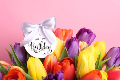 Image of Beautiful bouquet of tulip flowers with Happy Birthday card on pink background, closeup