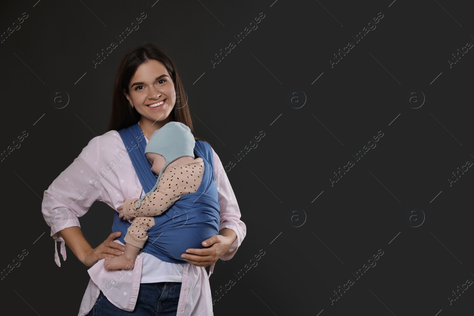 Photo of Mother holding her child in sling (baby carrier) on black background. Space for text