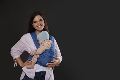 Mother holding her child in sling (baby carrier) on black background. Space for text