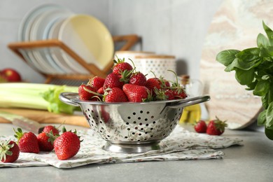 Metal colander with fresh strawberries on grey countertop in kitchen