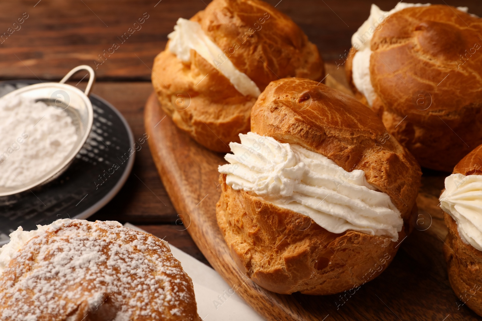 Photo of Delicious profiteroles with cream filling and powdered sugar on wooden table, closeup