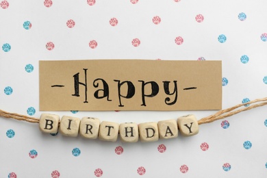 Card and wooden cubes with words HAPPY BIRTHDAY on paper with color pattern, flat lay